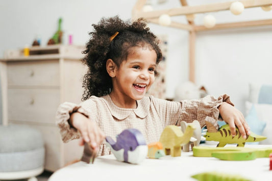 A little girl plays at a table with wooden dinosaurs